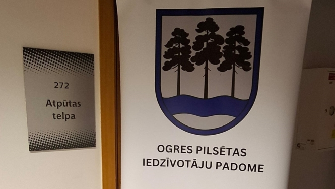 Pie 272. telpas ieejas durvīm novietots informatīvs stends ar Ogres pilsētas iedzīvotāju padomes kontaktinformāciju