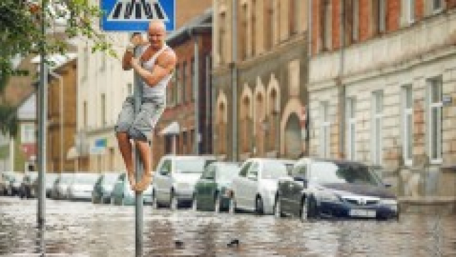 Vīrietis uz ceļazīmes staba applūdušā ielā