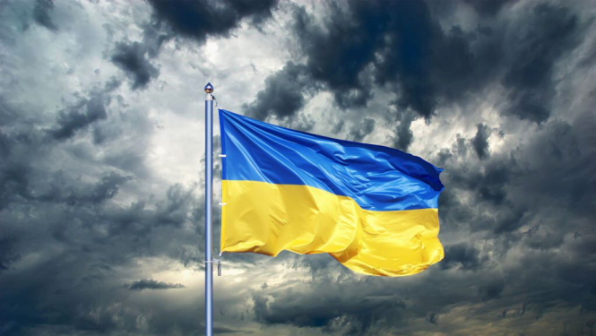 Vējā plīvojošs Ukrainas karogs uz mākoņainu debesu fona