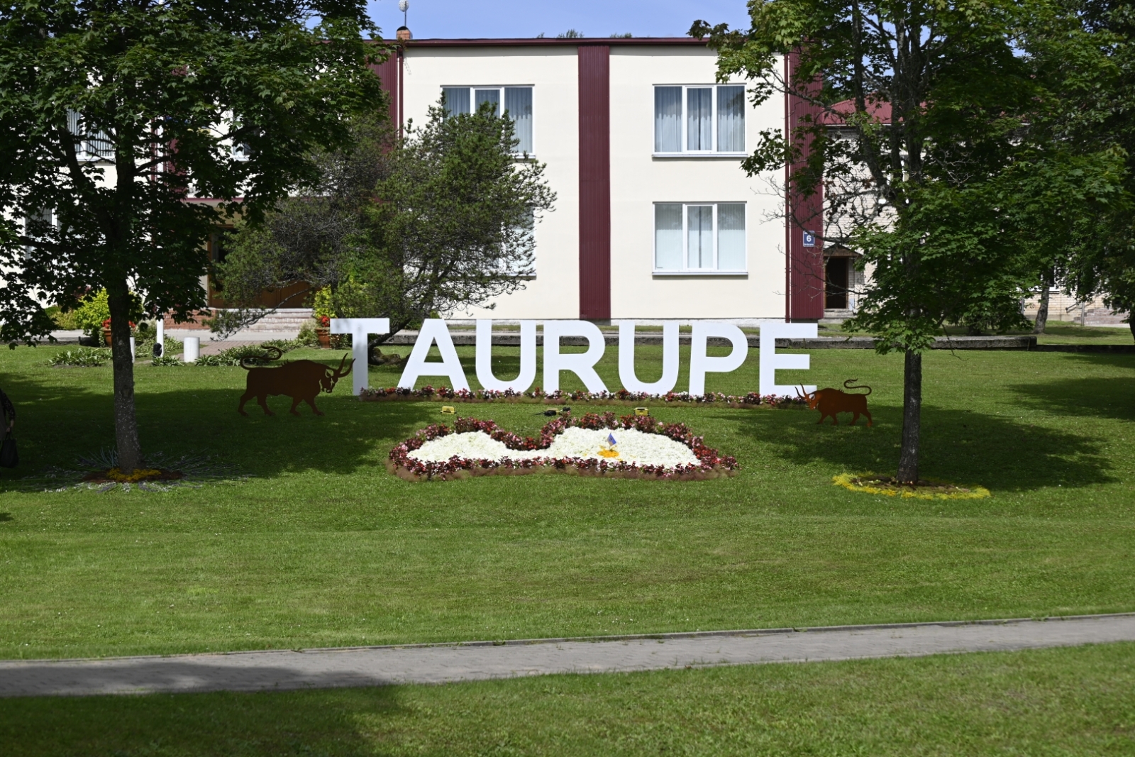 Taurupes pagasta pārvaldes ēka ar uzrakstu TAURUPE un no ziediem veidotu Latvijas kontūru priekšplānā