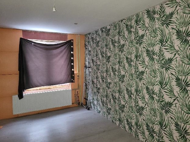 Istaba ar logu un sienu, kas klāta ar tapetēm zaļu lapu rakstā 