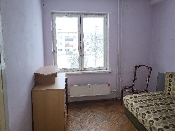 Istaba gaiši violetā tonī ar logu un dažām mēbelēm