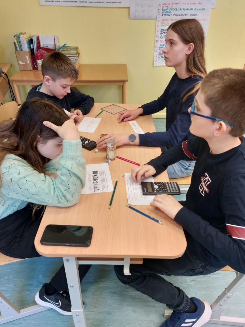 4 jaunieši pie galda risina uzdevumus