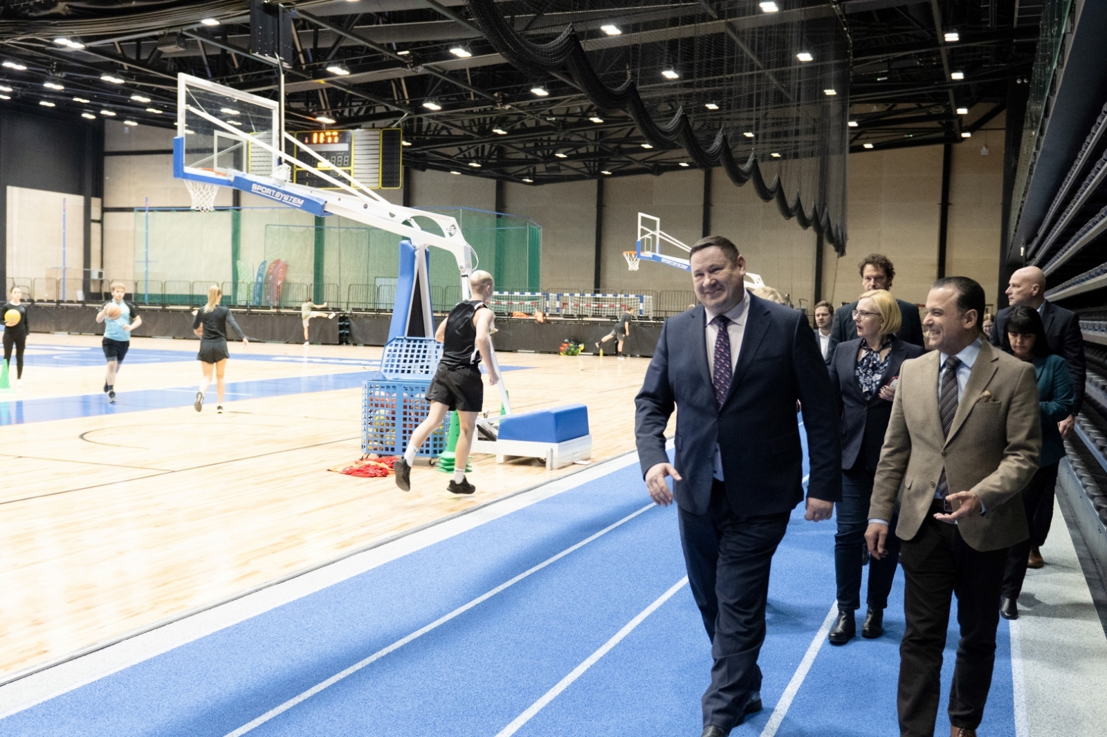 Tikšanās dalībnieki iet pa sporta arēnas skrejceļu