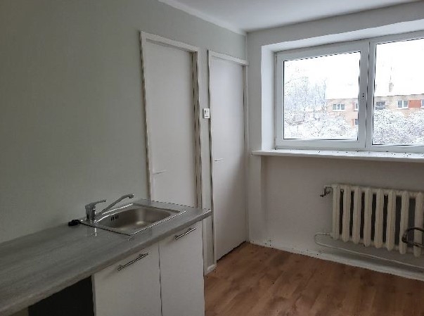 Virtuve gaišos toņos ar logu, radiatoru, izlietni un virtuves mēbelēm