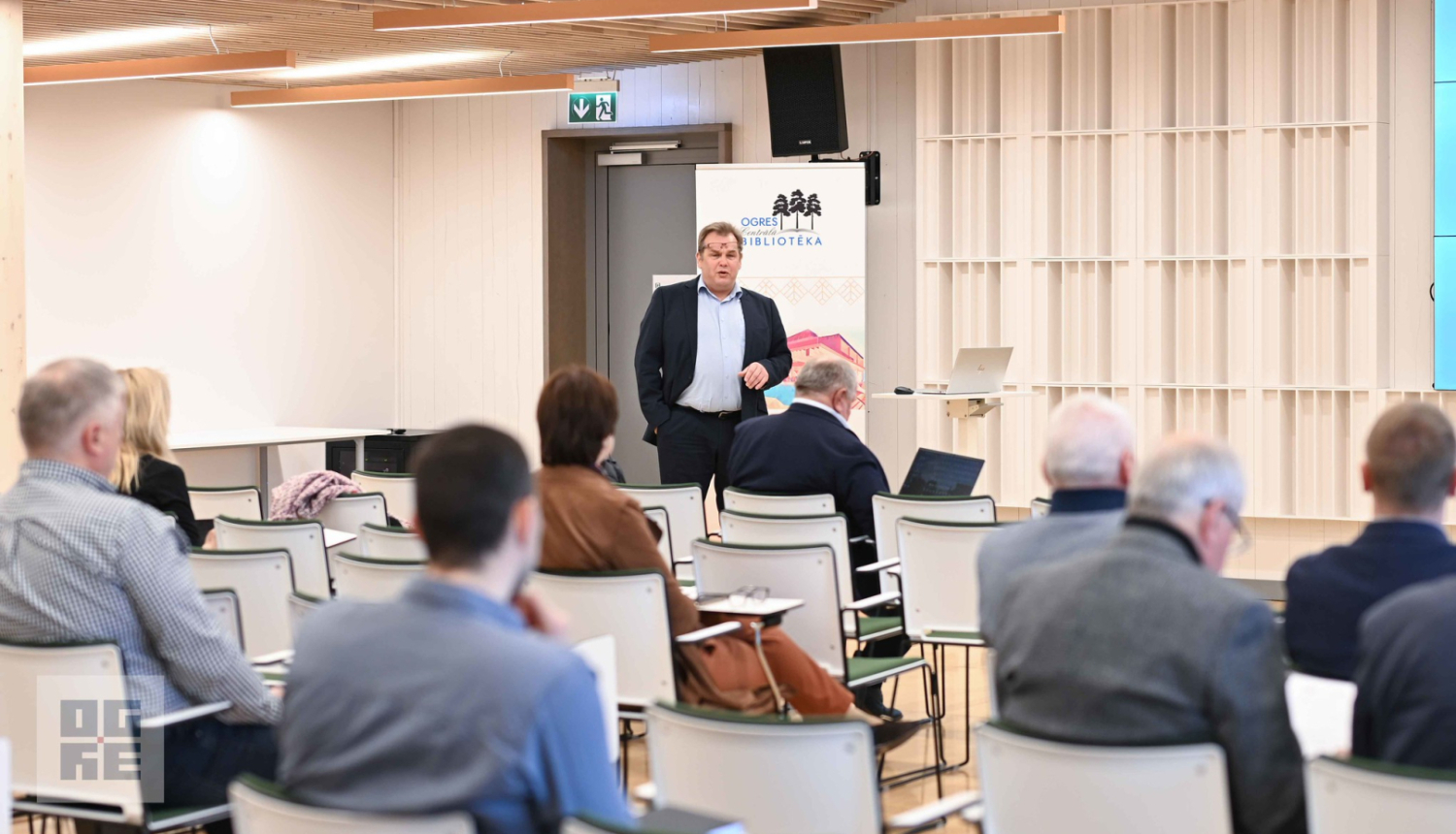 Semināra dalībnieki Ogres Centrālās bibliotēkas zālē klausās SIA “Latvijas standarts” valdes locekļa Ingara Pilmaņa stāstījumu