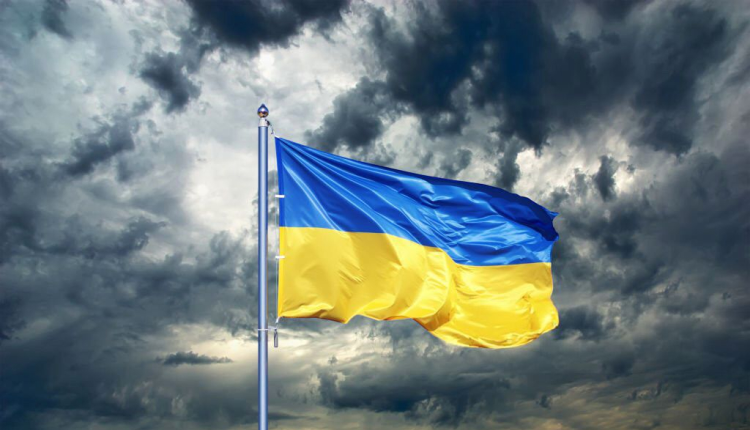 Vējā plīvojošs Ukrainas karogs uz mākoņainu debesu fona