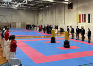 Ogrē norisinājās 24. Starptautiskais karatē turnīrs „Ogre Karate Cup & Games 2026”. Atklāšana. Laukuma vienā pusē stāv tiesneši, otrā - dalībnieki.