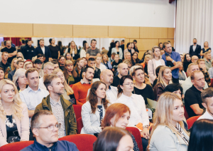 Ķeguma pamatskolā atklāta “zaļā klase” – jauna āra telpa skolēniem un kopienai. Vecāki zālē uzklausa prezentāciju