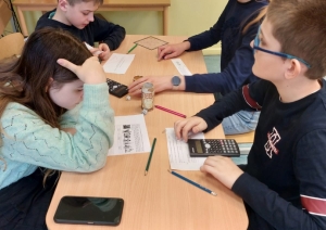 4 jaunieši pie galda risina uzdevumus