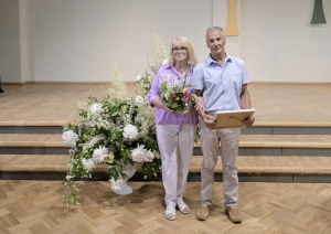 Vīrietis baltā kreklā, gaišās biksēs, sieviete rozā blūzē, gaišās biksēs Ogres novada Zelta kāzu pāris 31.05.2024