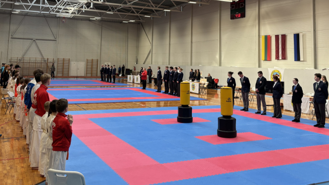 Ogrē norisinājās 24. Starptautiskais karatē turnīrs „Ogre Karate Cup & Games 2026”. Atklāšana. Laukuma vienā pusē stāv tiesneši, otrā - dalībnieki.