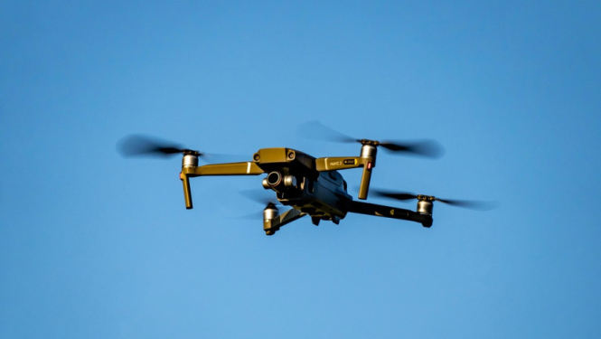 Attēls rakstam par iespējām apgūt dronu pilotēšanu. Attēlā lidojošs drons uz zilas debess fona