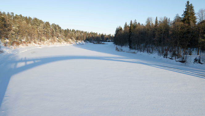 Ogres upe ziemā, ēnā uz ledus atspīd gājēju tilts
