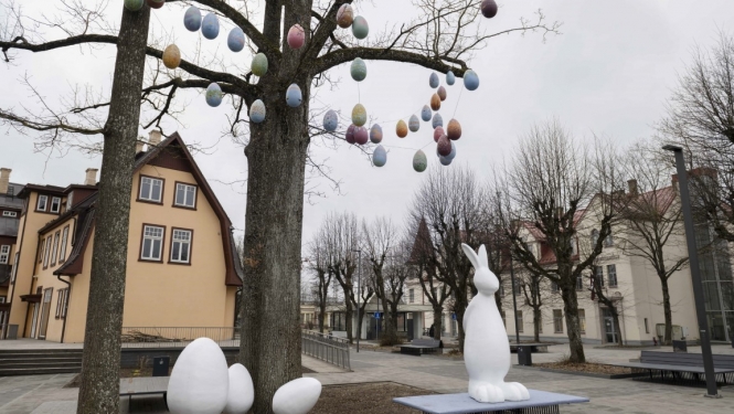 Balts Lieldienu zaķis ar olām pie koka, zaros iekārtas mazas olas
