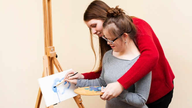 Sieviete palīdz meitenei ar īpašām vajadzībām gleznot
