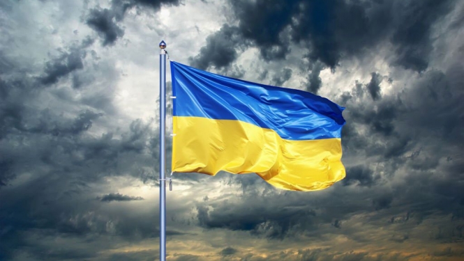 Vējā plīvojošs Ukrainas karogs uz mākoņainu debesu fona