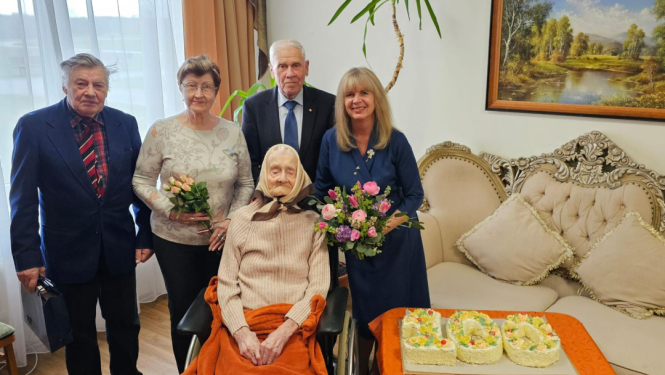 Deputāte Sarmīte Ozoliņa un Ogres politiski represēto kluba biedri kopā ar jubilāri Malvīni Asari, līdzās - torte, kas veidota formā "100"