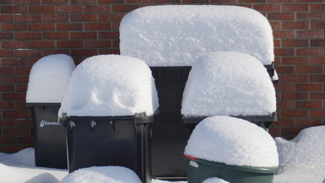 Apsniguši atkritumu konteineri pie ķieģeļu sienas