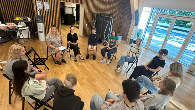 Dienas nodarbības Ogres Jauniešu mājā par brīvprātīgo darbu – jaunieši atklāj motivāciju, līderību un pārliecību par saviem spēkiem. Attēlā jaunieši sēž aplī un apgūst jaunās zināšanas