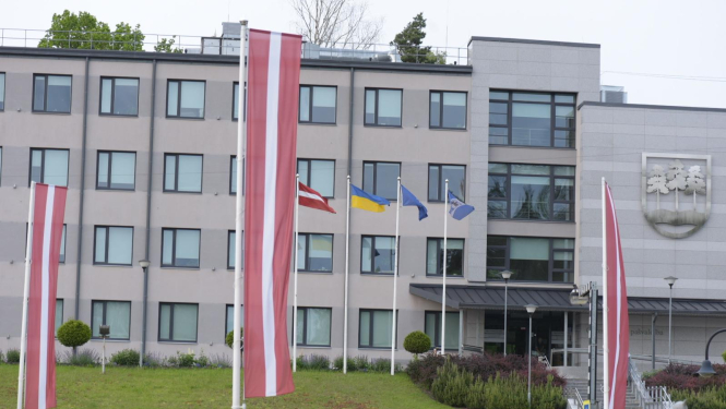 Ogres novada pašvaldības domes ēka 2025. gada pavasarī. Priekšplānā Latvijas sarkanbaltsarkanie karogi