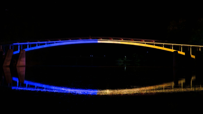 Ukrainas karoga krāsās izgaismotais gājēju tilts pār Ogres upi