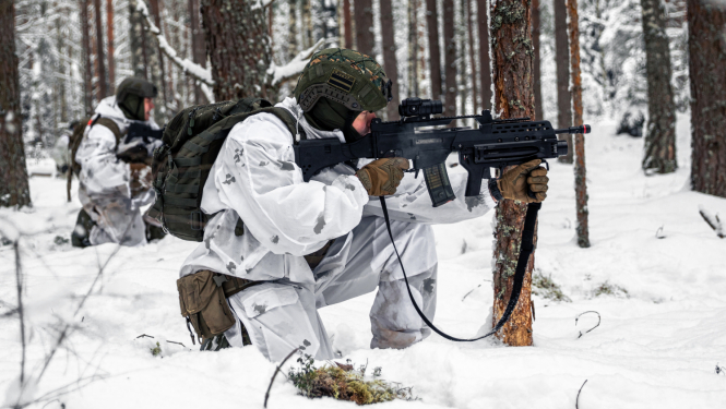 Divi karavīri baltos aizsargtērpos ar ieročiem mācību laikā mežā ziemas apstākļos