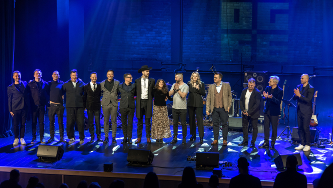 Skatuves mākslinieku kopbilde - 15 mūziķi koncerta noslēgumā nostājušies vienā taisnā līnijā uz Ogres novada Kultūras centra skatuves