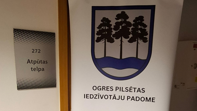 Pie 272. telpas ieejas durvīm novietots informatīvs stends ar Ogres pilsētas iedzīvotāju padomes kontaktinformāciju