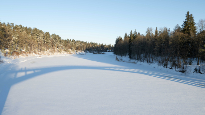 Ogres upe ziemā, ēnā uz ledus atspīd gājēju tilts