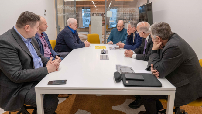 Tikšanās dalībnieki pie apspriežu galda klausās vēsturnieka stāstījumu