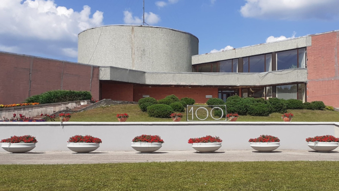 Madlienas pagasta pārvaldes ēka ar dekoratīvajiem puķu podiem un uzrakstu 100