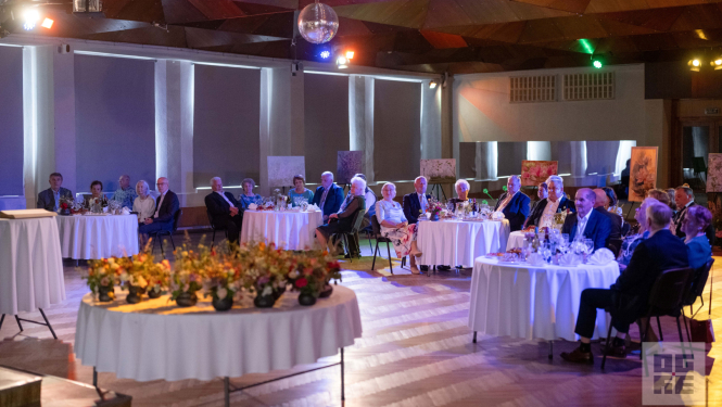 7. jūnijā Ogres novada Kultūras centrā svinīgā gaisotnē notika Ogres novada stipro pāru godināšanas pasākums – tika sveikti pāri, kuri laulībā nodzīvojuši 50 un 60 gadus. Priekšplānā galds ar īpaši darinātiem māla traukiem katram pārim. Pāri sēž pie galdiņiem un bauda sveikšanas pasākumu.