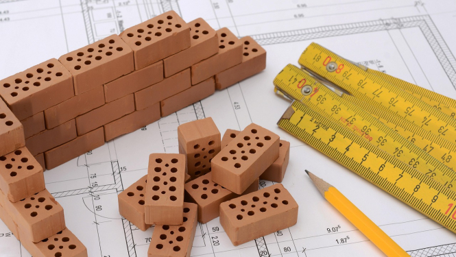 Būvniecības darbi Ogres novadā. Attēlā rasējums mērlenta, zīmulis un ķieģeļi