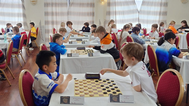 Sacensības dambretē Polijā, spēlē divi zēni. 11.2023.