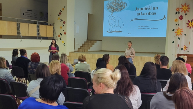 Cilvēki redzami ar mugurām, sēž krēslos, priekšā pasniedzējs stāsta par atkarību izraisošām vielām. 25.09.2024.