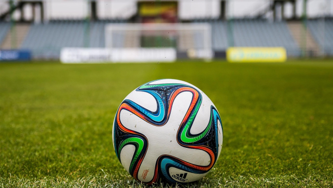 Futbola bumba stadionā ar mākslīgās zāles segumu zaļā krāsā. Fonā tribīnes.