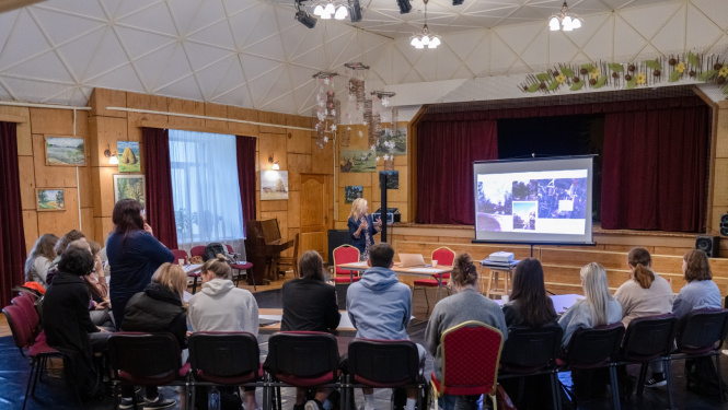 Ķeipenes tautas namā studenti sēž pie galda, fonā prezentācija 11.09.2024.