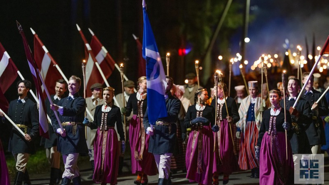 Lāpu gājiens Ogrē par godu Lāčplēša dienai. Priekšplānā jaunieši tautas tērpos, rokās nesot Ogres karogu un Latvijas karogus