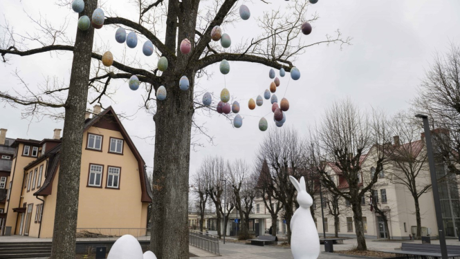 Balts Lieldienu zaķis ar olām pie koka, zaros iekārtas mazas olas