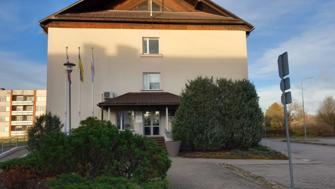 Lielvārdes pilsētas un pagasta pārvaldes ēka ar karogu mastiem un skujeņu stādījumiem priekšplānā