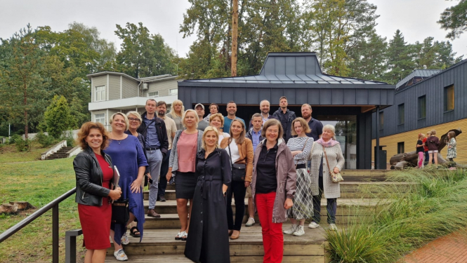 Pasākuma dalībnieki stāv uz Ogres Centrālās bibliotēkas kāpnēm