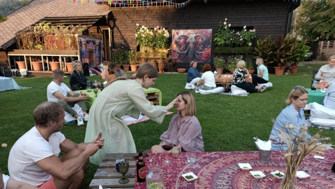 Cilvēki sēž pie galdiem, tiek krāsotas sejas 