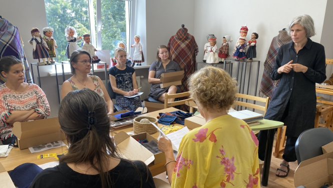 Nodarbību dalībnieces sēž ap galdu un klausās nodarbību vadītājas teikto