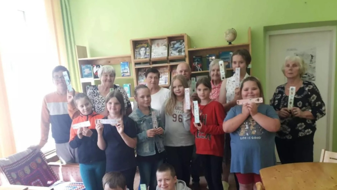 Seniori ar jauniešiem stāv ar dažādiem pašu veidotiem priekšmetiem rokās 08.2024.