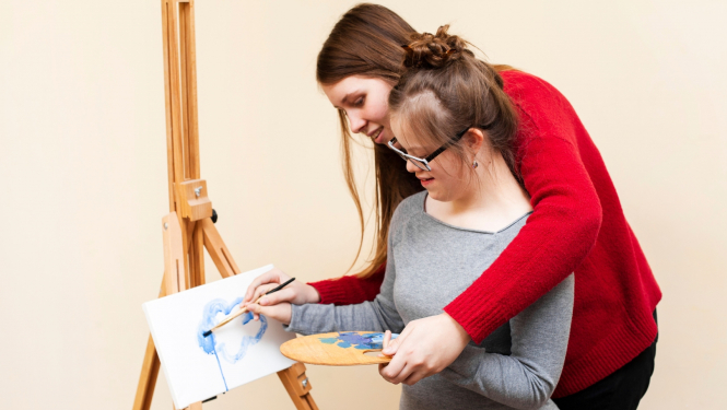 Sieviete palīdz meitenei ar īpašām vajadzībām gleznot