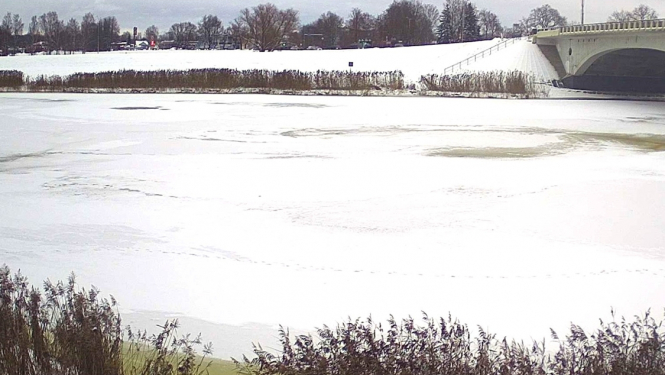 Upe noklāta ar ledu, fonā tilts