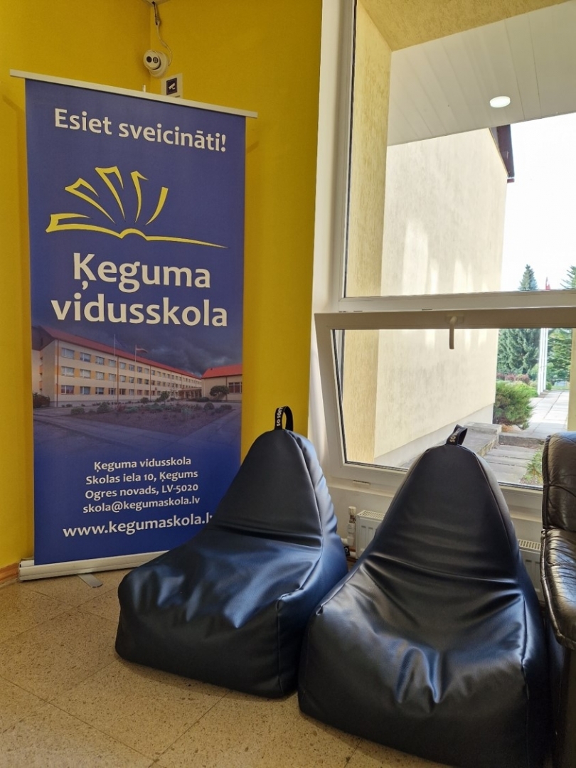 2 pufi un plakāts ar uzrakstu "Esiet sviecināti! Ķeguma vidusskola"