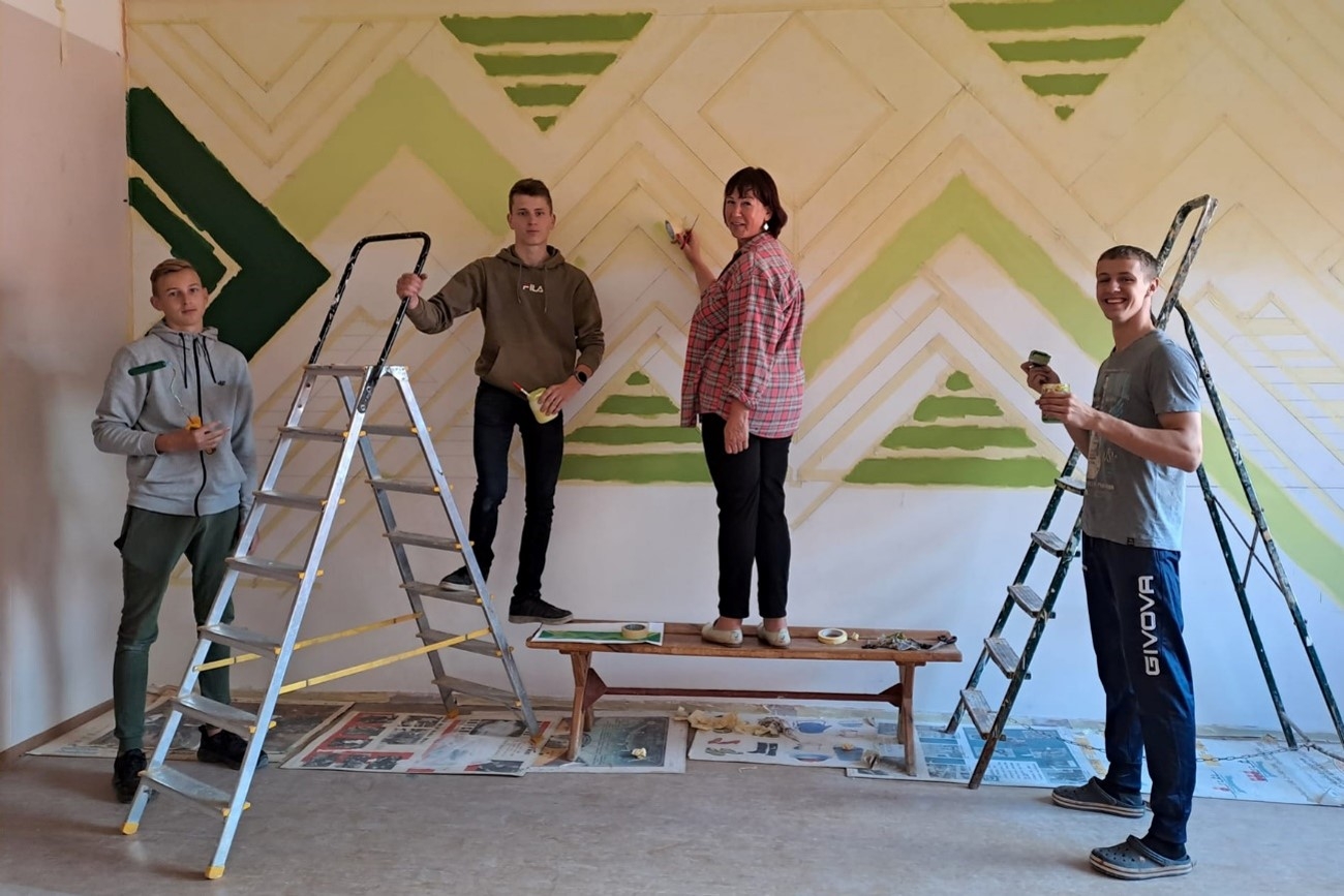 3 skolēni un skolotāja zīmē sienu gleznojumu skolas vestibilā
