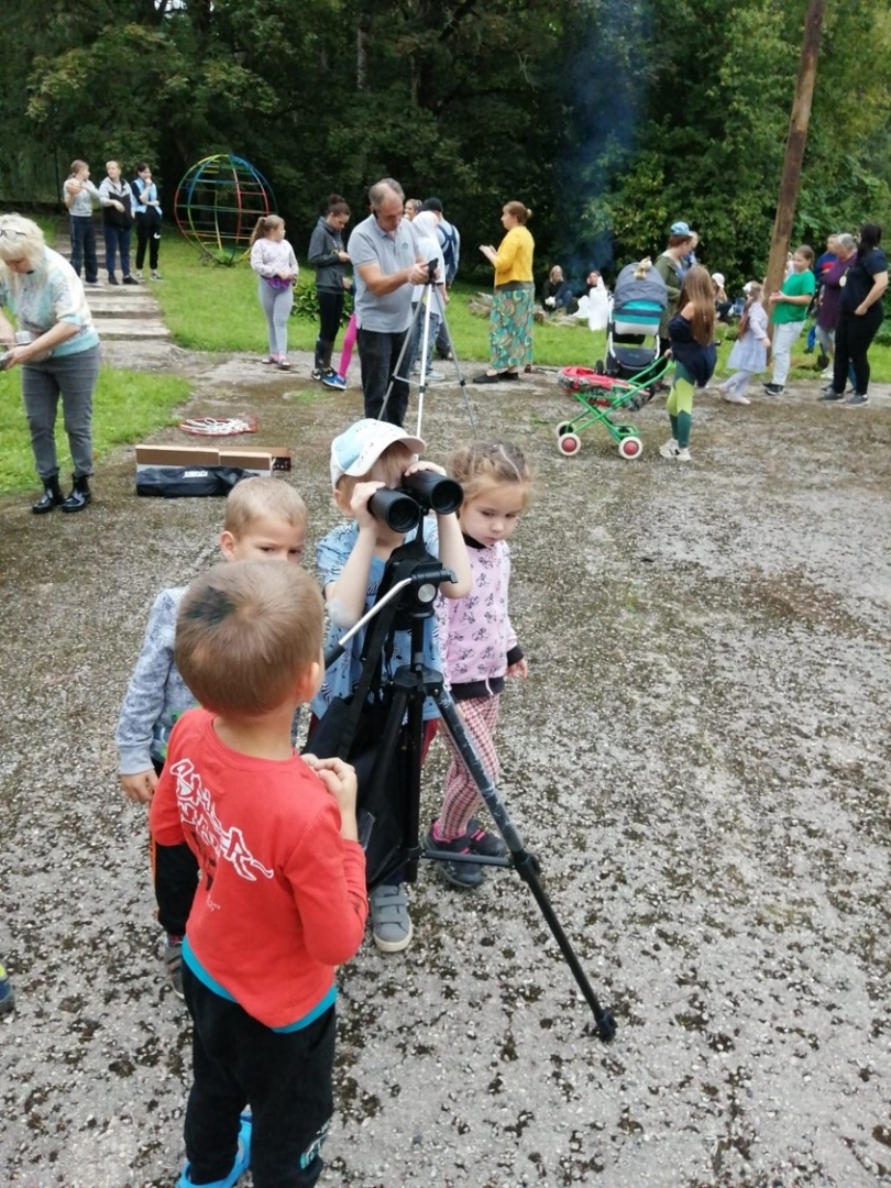 Bērni ar binokli vēro dabu bērnudārza teritorijā notiekošā pasākumā